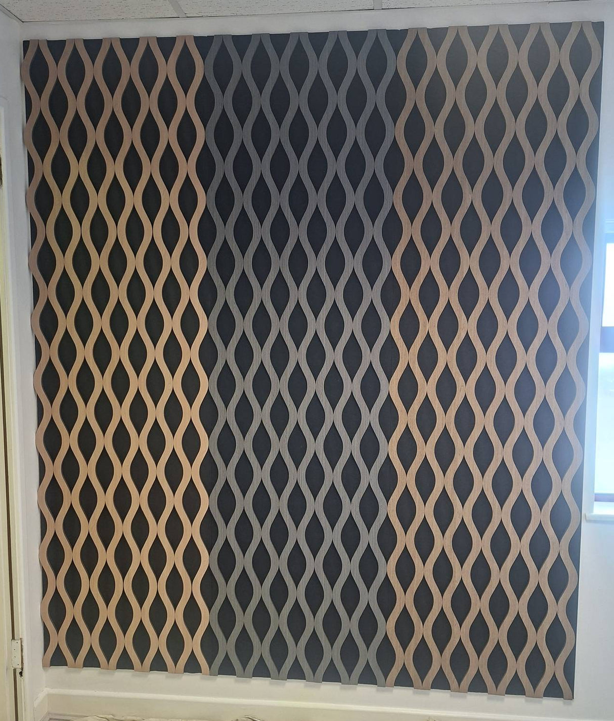 A large wall panel featuring a repeating diamond lattice pattern in beige and dark charcoal gray, installed on a wall in an interior room