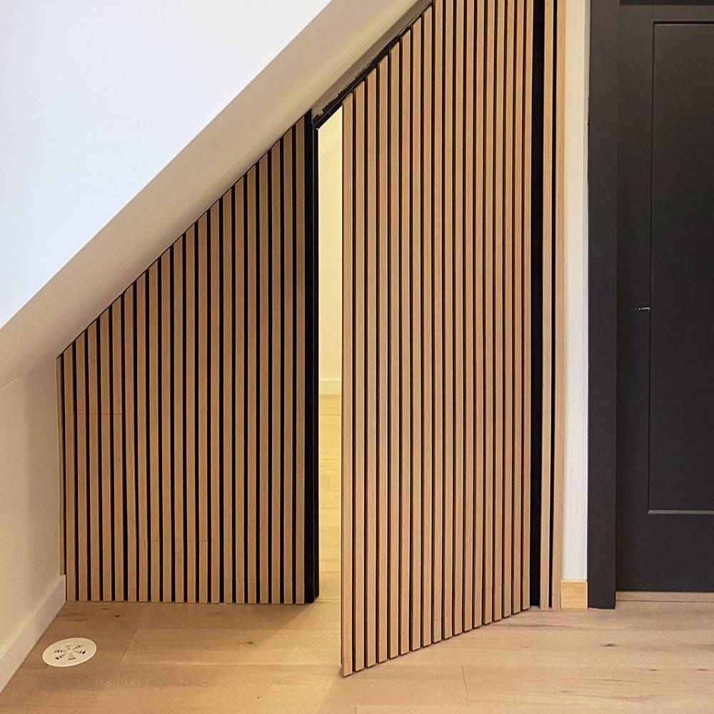 Wooden slatted interior doors installed along a staircase, shown partially open to reveal a room beyond, in a modern home interior.