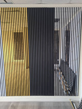 A modern wall-mounted slatted screen or partition panel with three vertical sections: white, black, and gold, installed in an indoor space with wood-look flooring.