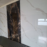 Large-format wall tiles shown in a showroom setting, featuring a white marble-look pattern with gray veining on the right and a dark brown and black marble-look panel on the left.