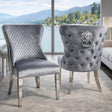 Two gray velvet dining chairs with silver metal legs, shown in a modern living room setting with a large window overlooking water and mountains.