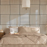A styled bedroom scene featuring a bed dressed in beige quilted bedding and pillows, set against a bold geometric wallpaper with black and beige stripes. A matching patterned rug covers the floor, and a wooden nightstand with a lamp is visible on the left.