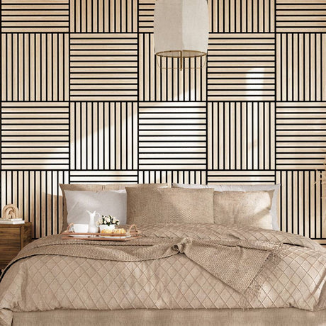 A styled bedroom scene featuring a bed dressed in beige quilted bedding and pillows, set against a bold geometric wallpaper with black and beige stripes. A matching patterned rug covers the floor, and a wooden nightstand with a lamp is visible on the left.