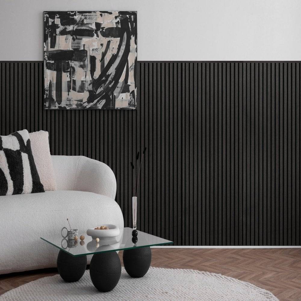 A modern living room corner featuring a white curved sofa with a black-and-white patterned pillow, a small glass-top coffee table with black spherical legs, a black ribbed accent wall, and abstract black, white, and gray wall art above.