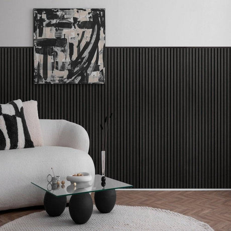 A modern living room corner featuring a white curved sofa with a black-and-white patterned pillow, a small glass-top coffee table with black spherical legs, a black ribbed accent wall, and abstract black, white, and gray wall art above.
