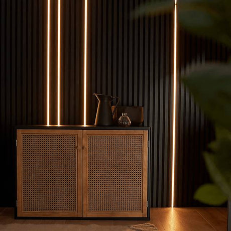 A modern wooden sideboard cabinet with two woven cane doors, styled with dark ceramic vessels against a dark wood slatted wall with vertical LED light strips.