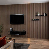 A modern living room featuring a dark brown wood slat accent wall with a vertical LED light strip. A black flat-screen TV and floating black shelves are mounted on the wall above a light wood floor.
