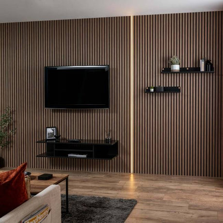 A modern living room featuring a dark brown wood slat accent wall with a vertical LED light strip. A black flat-screen TV and floating black shelves are mounted on the wall above a light wood floor.