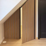 Wooden slatted interior doors installed along a staircase, shown partially open to reveal a room beyond, in a modern home interior.